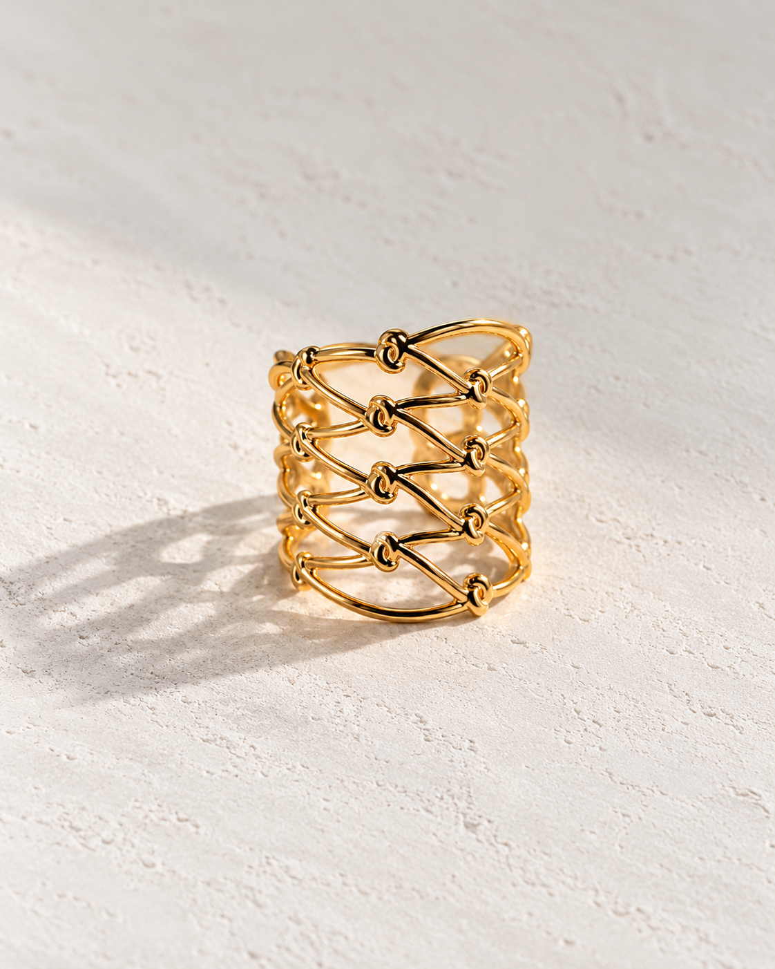 Anillo Sidonie dorado de entramado sobre cemento blanco